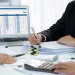 A diverse group of business professionals collaborates on a laptop, discussing client bookkeeping solutions for small businesses.